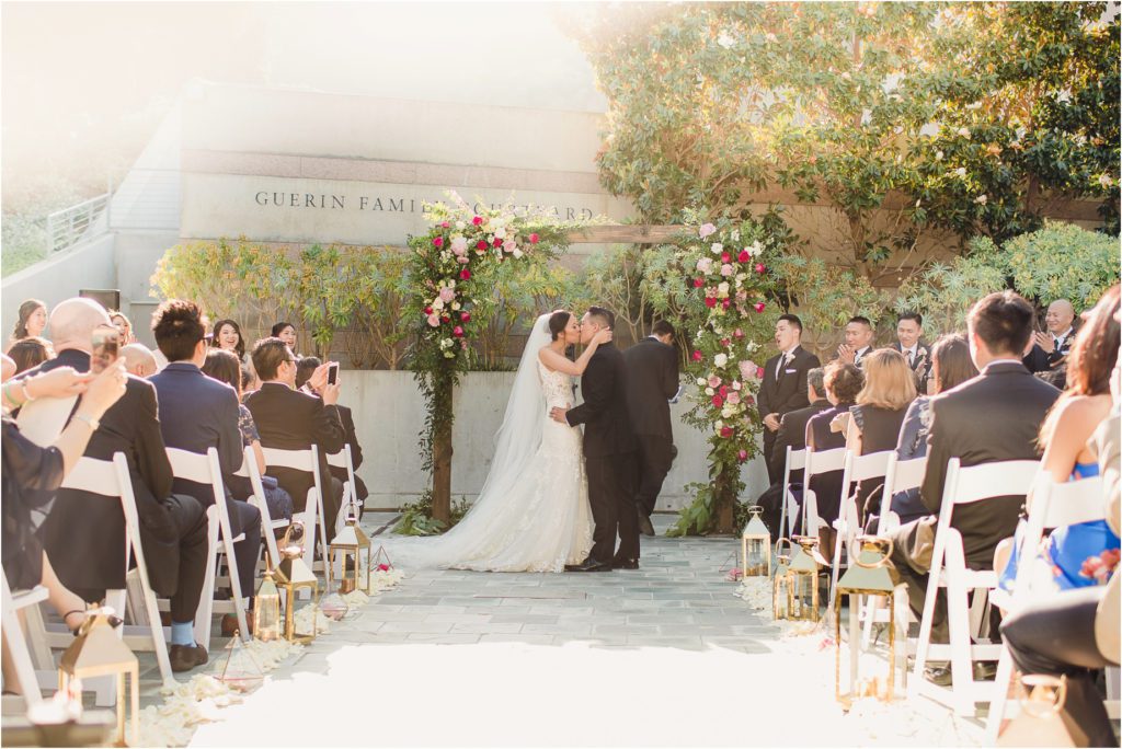 A wedding at the Skirball Cultural Center. The bride and groom stand at the end of the aisle as their guests took on