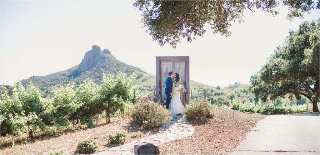 A bride and groom pose in front of the door that leads to nowhere at their Saddlerock Ranch wedding