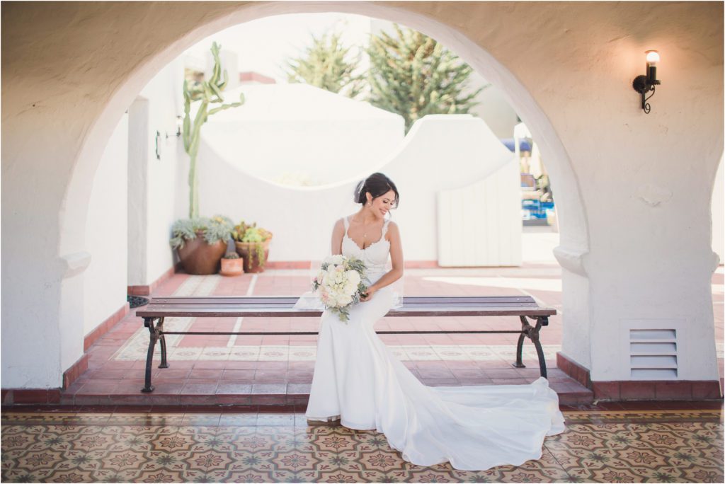 A bride sits on a bench under an arch at Casa Romantica in San Clemente