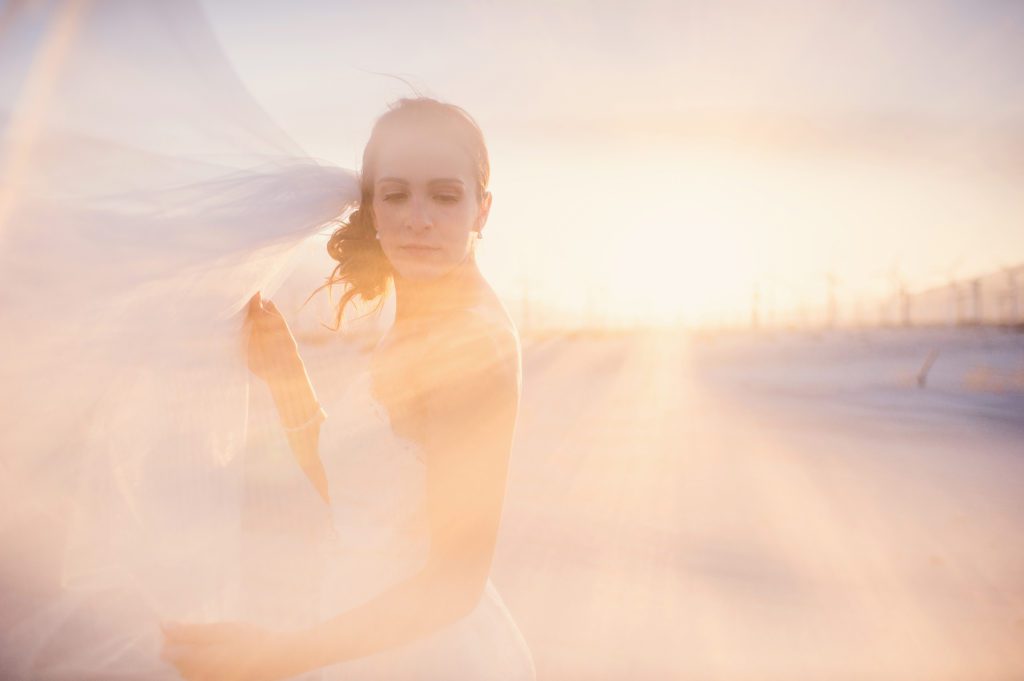A bride poses in front of windmills at sunset during her Palm Springs Wedding
