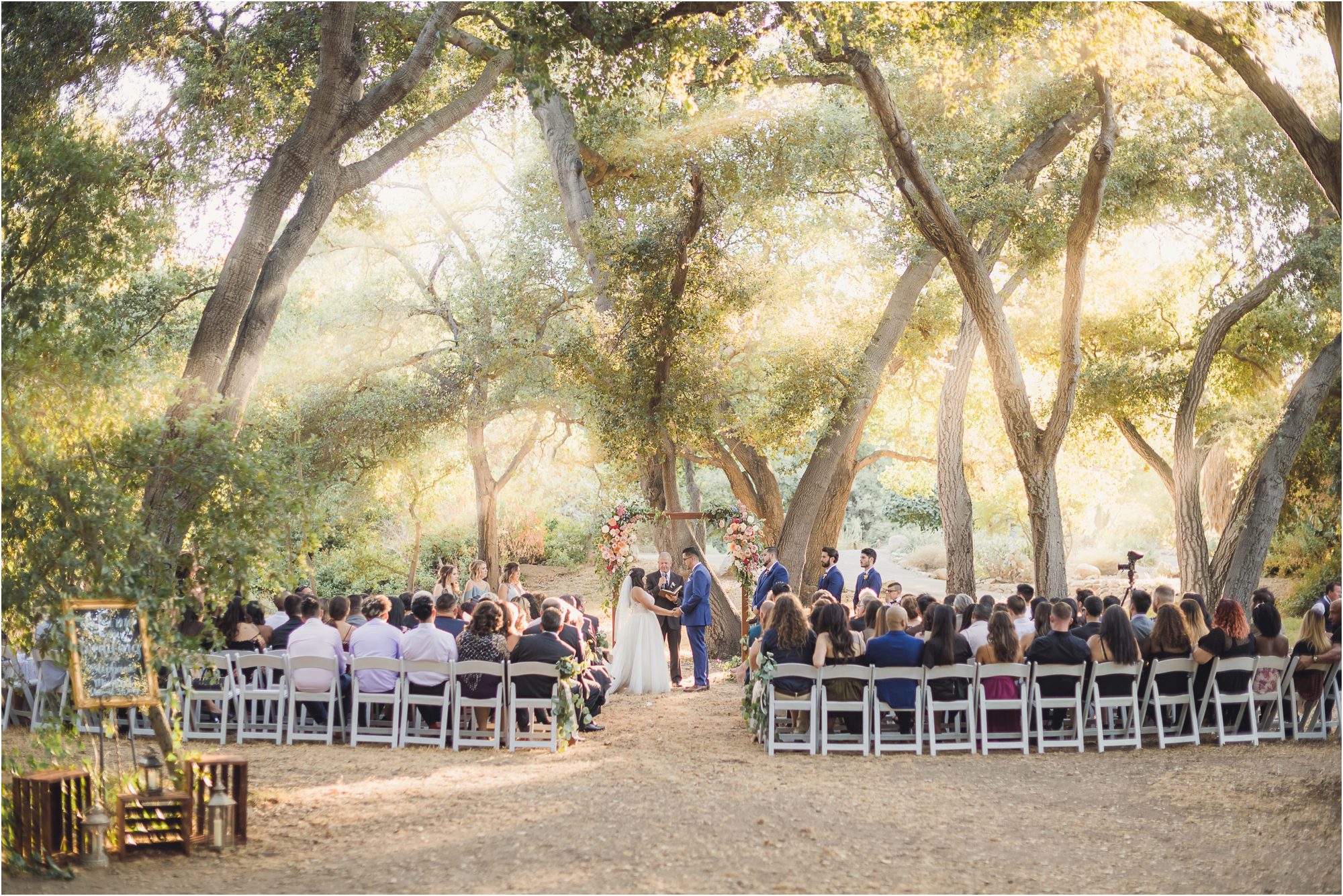 Michael and Stephanie face each other at the end of the aisle, surrounded by an oak forest at their Fairytale Forest Wedding in Pasadena