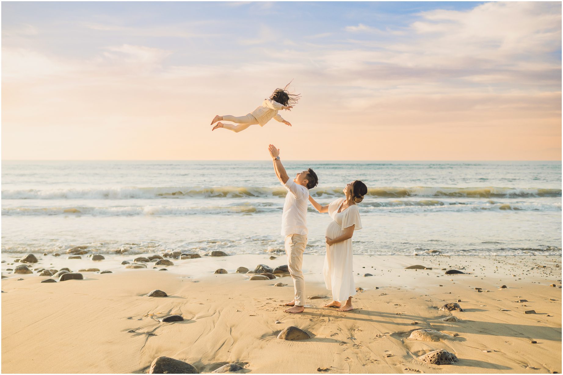 A father tosses his child as his wife looks on at Malaga Beach during their Holiday mini Sessions