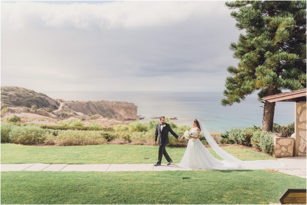 Samanta and James hold hands at a cliffside pacific Ocean view during their Wayfarers Chapel Wedding