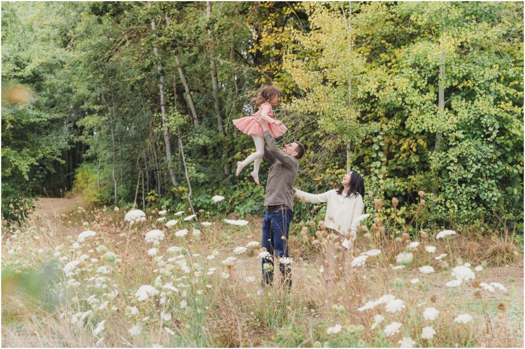 A Father tosses his daughter in the air as his wife looks on in this magical Tigard Family Photo Shoot at Dirksen Nature Park