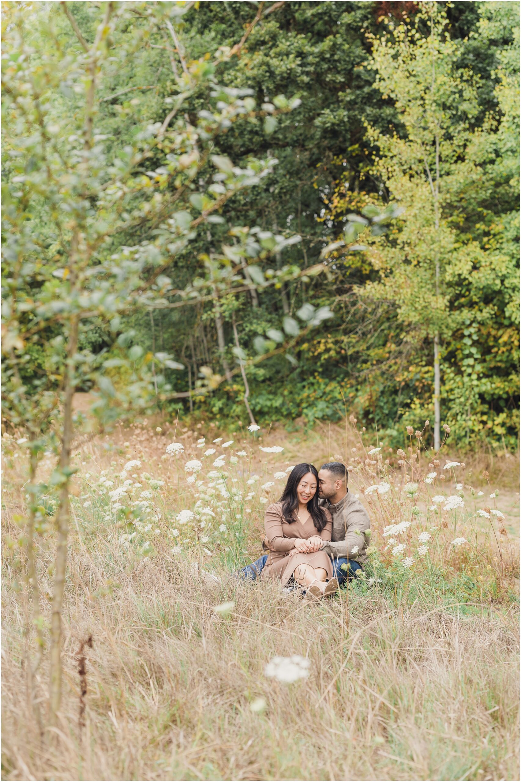 A couple sits in a field in Tigard during their Family Photo Shoot with Sun and Sparrow Photography