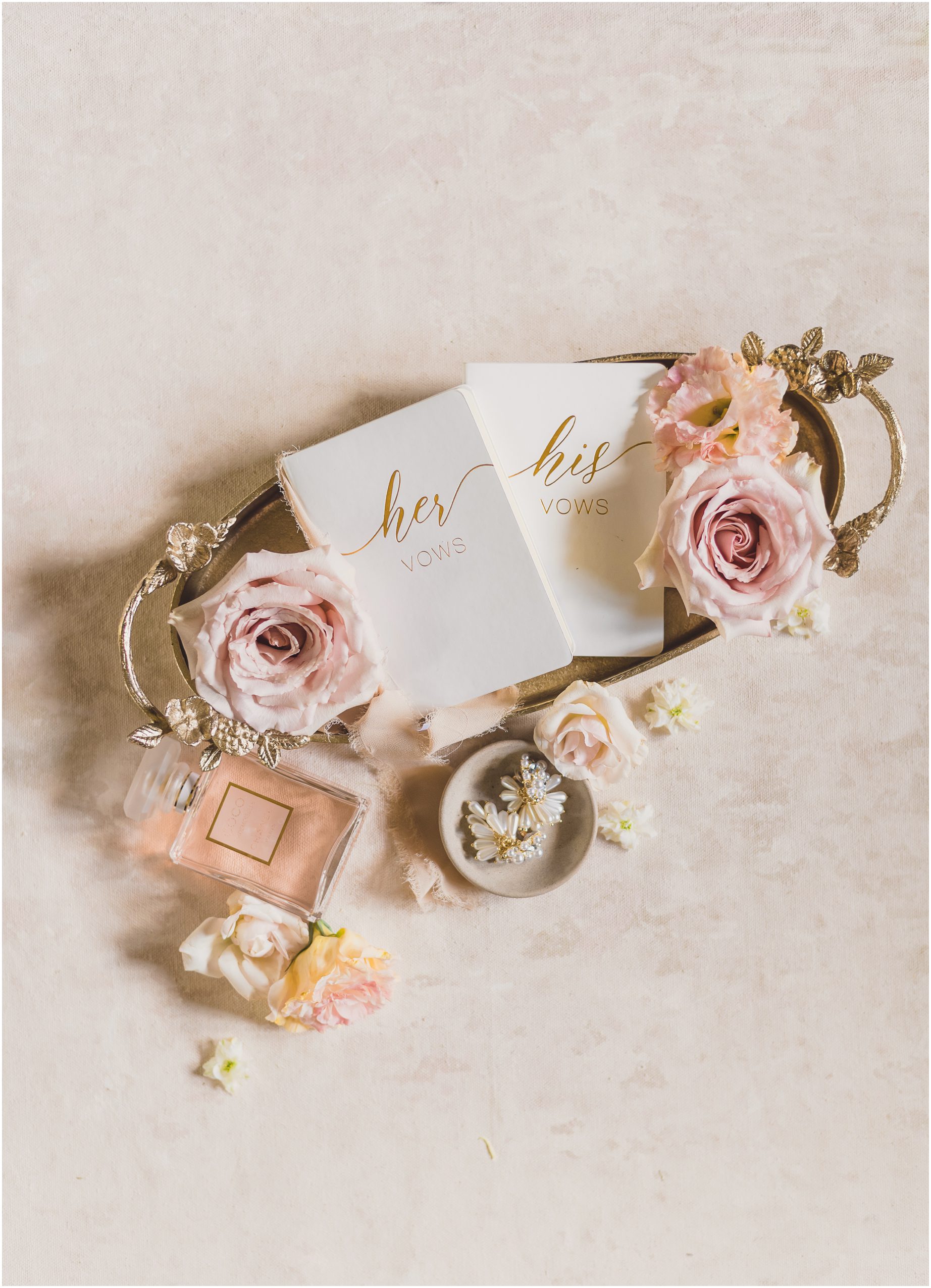 wedding details for a wedding in Southern California, featuring perfume, vow cards, pink flowers, white earrings, and a golden plate