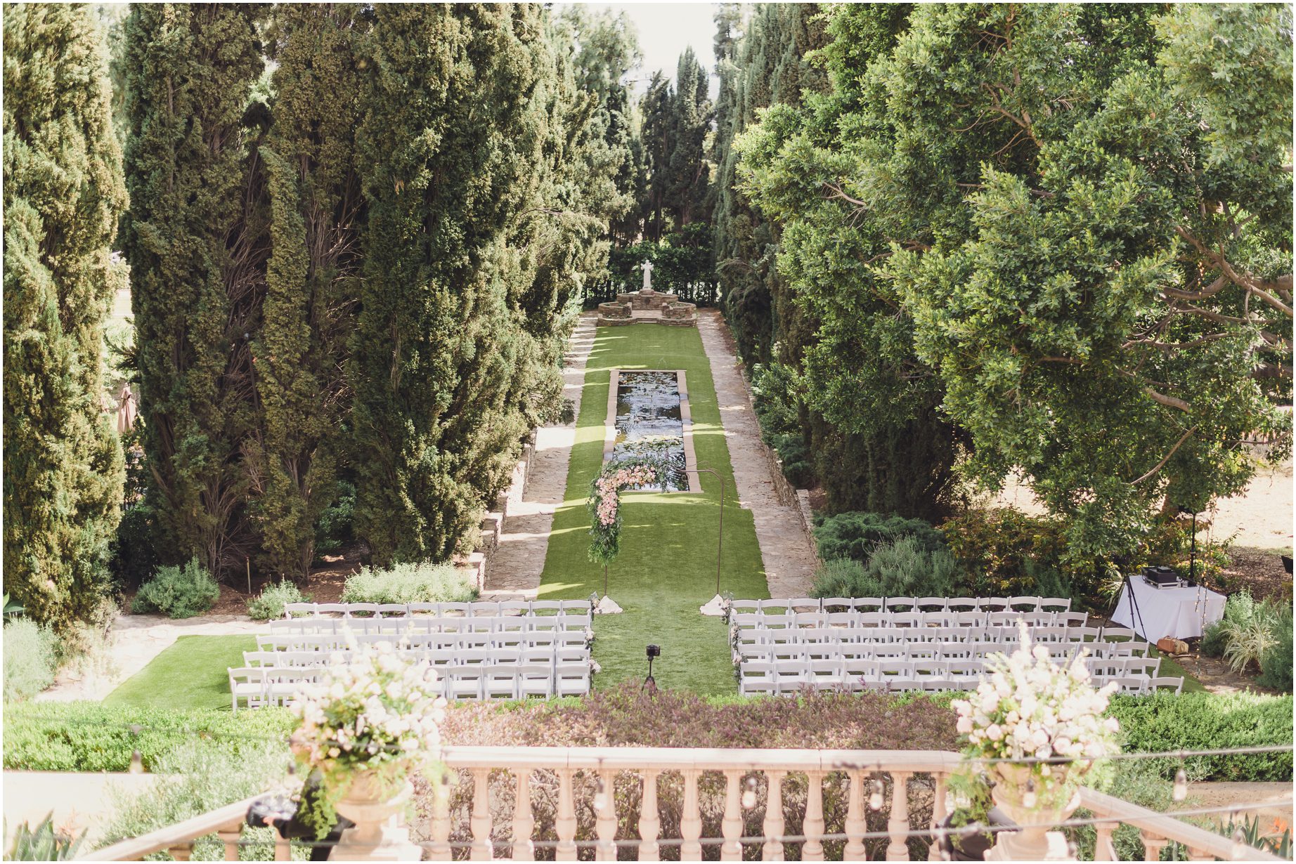 this ceremony space is set up beside a beautiful pond and a pathway lined in cypress trees