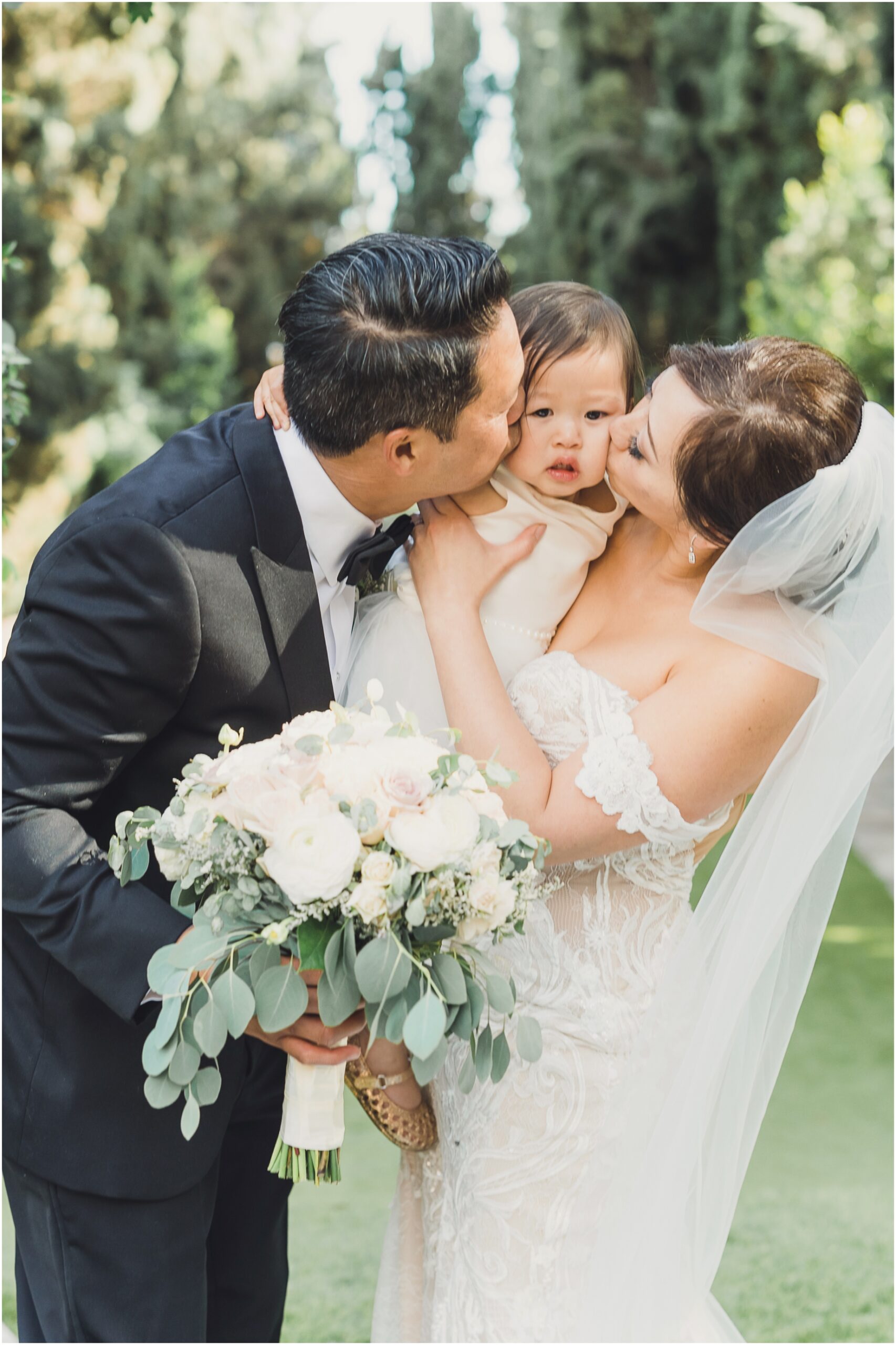 a bride and groom kiss their daughter on their wedding day