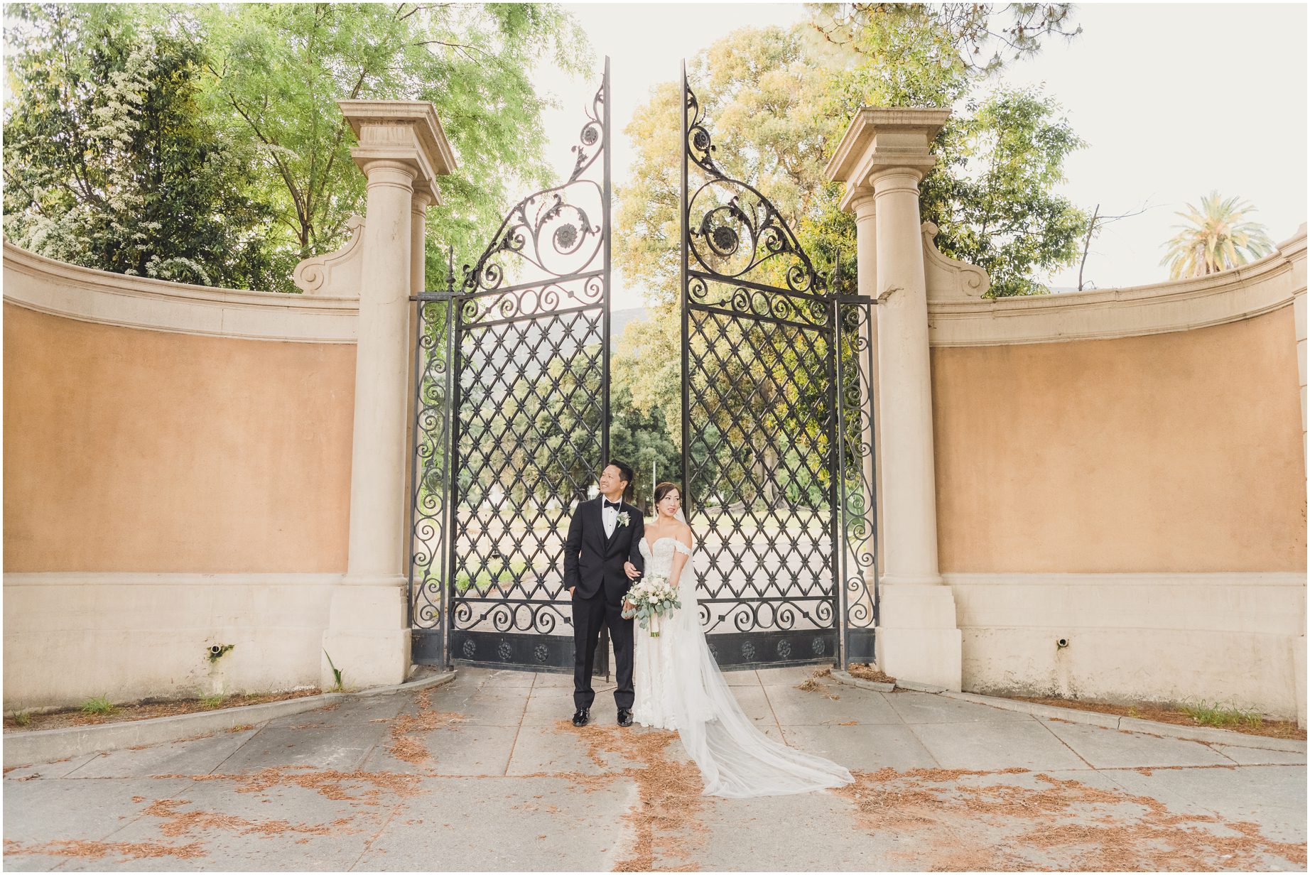 the bride and groom stand near a large fairytale-like gate