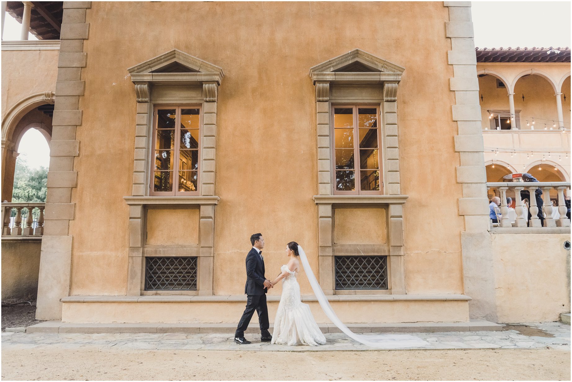 This is a dramatic shot of a bride and groom walking together near a building during their wedding at villa del sol d'Oro