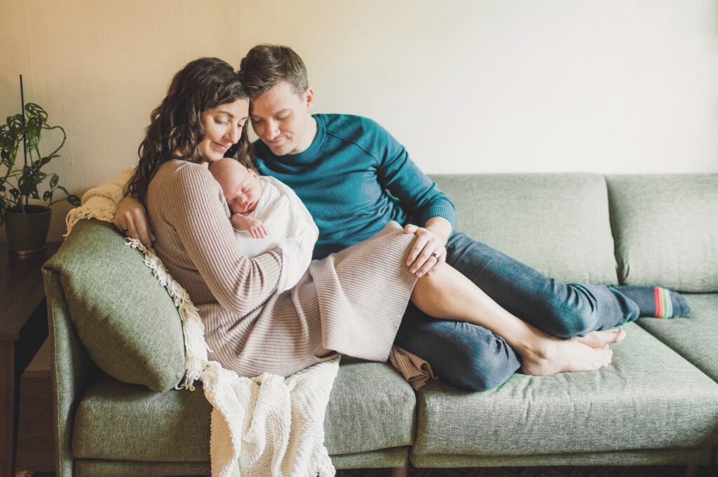 A new mother and father sit on the couch with their newborn for some Portland in-home newborn photography