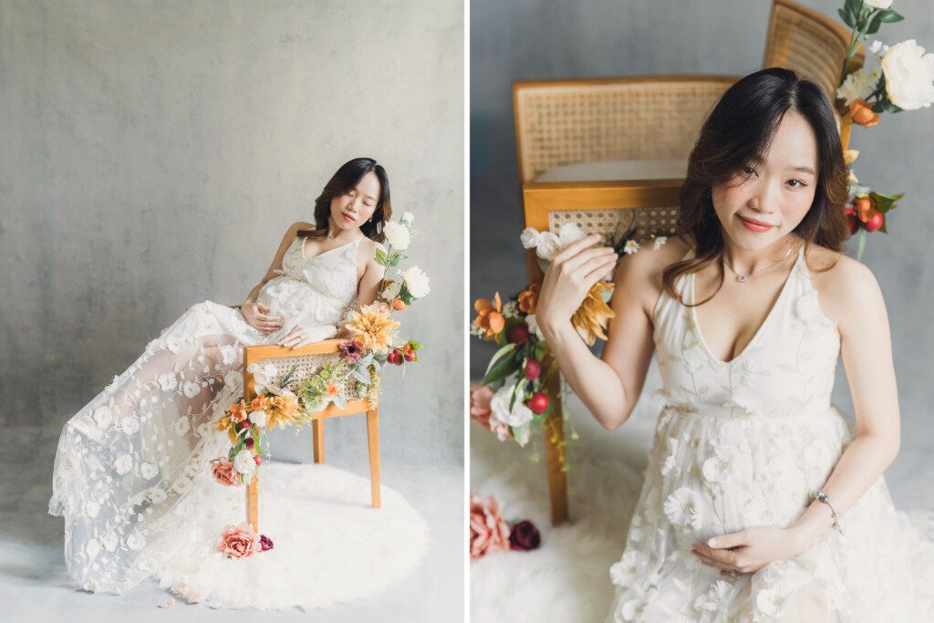 A pregnant woman sits in a chair with florals all around her while wearing a white dress