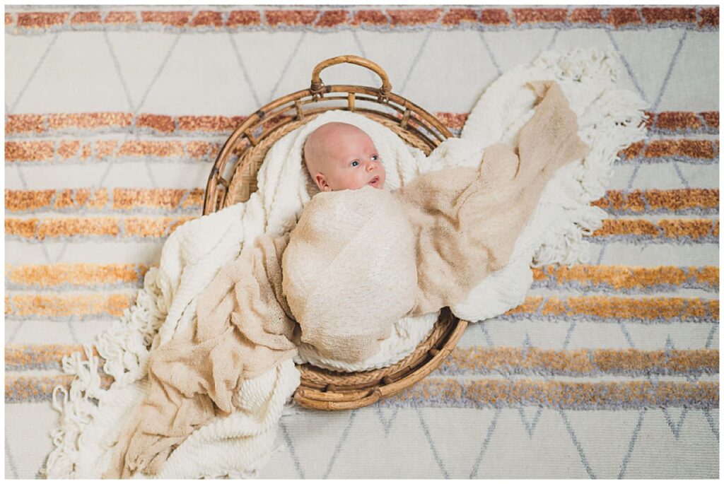 Portland Maternity and Newborn Photographer, sun and sparrow, took this photograph of a newborn baby in a basket, looking around from a bed of blankets, resting in a basket