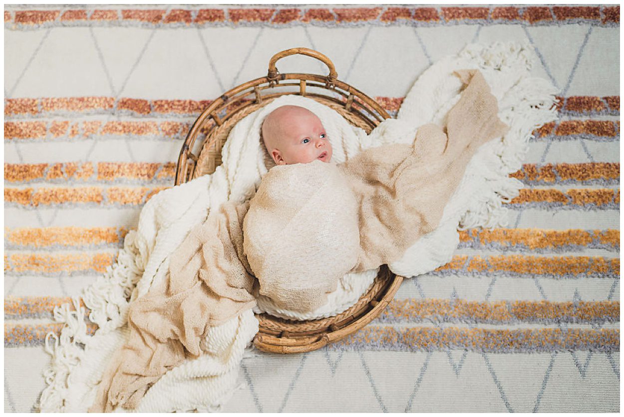 A wide eyed newborn lays in a basket, wrapped in blankets that sprawl out diagonally left to right. un and sparrow is a Portland Newborn Photographer