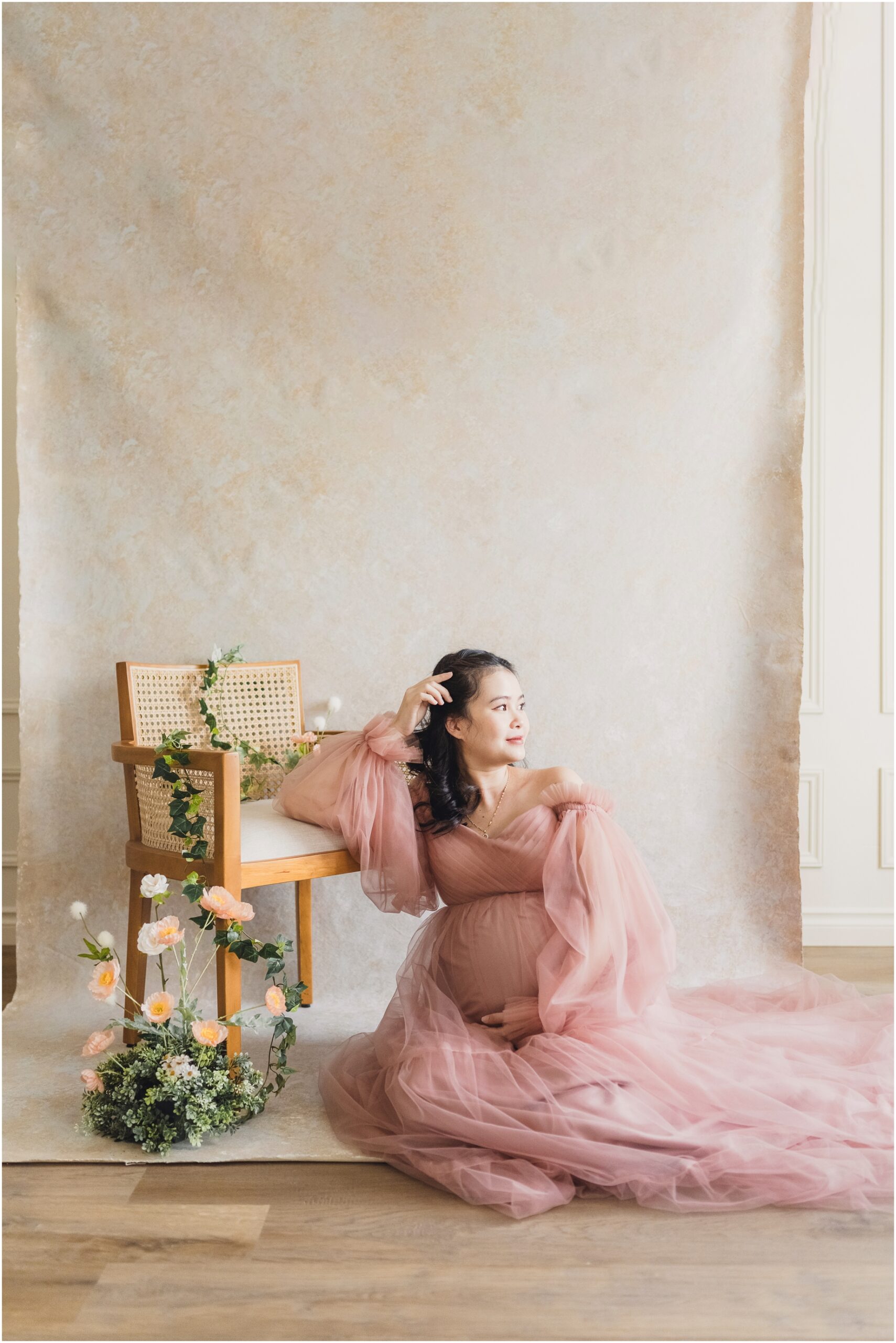 A woman at her Maternity Session in Vancouver Washington looks into the light as she leans on a chair covered in flowers