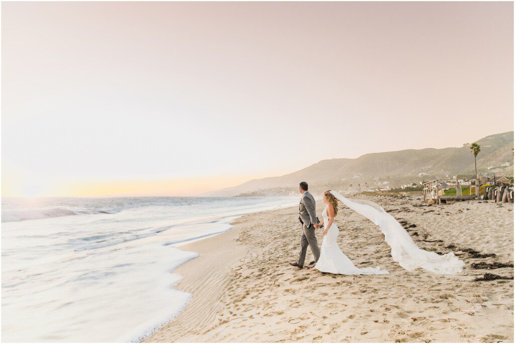 A bride and groom walk toward the waves during their sunset beach wedding at Malibu west beach club