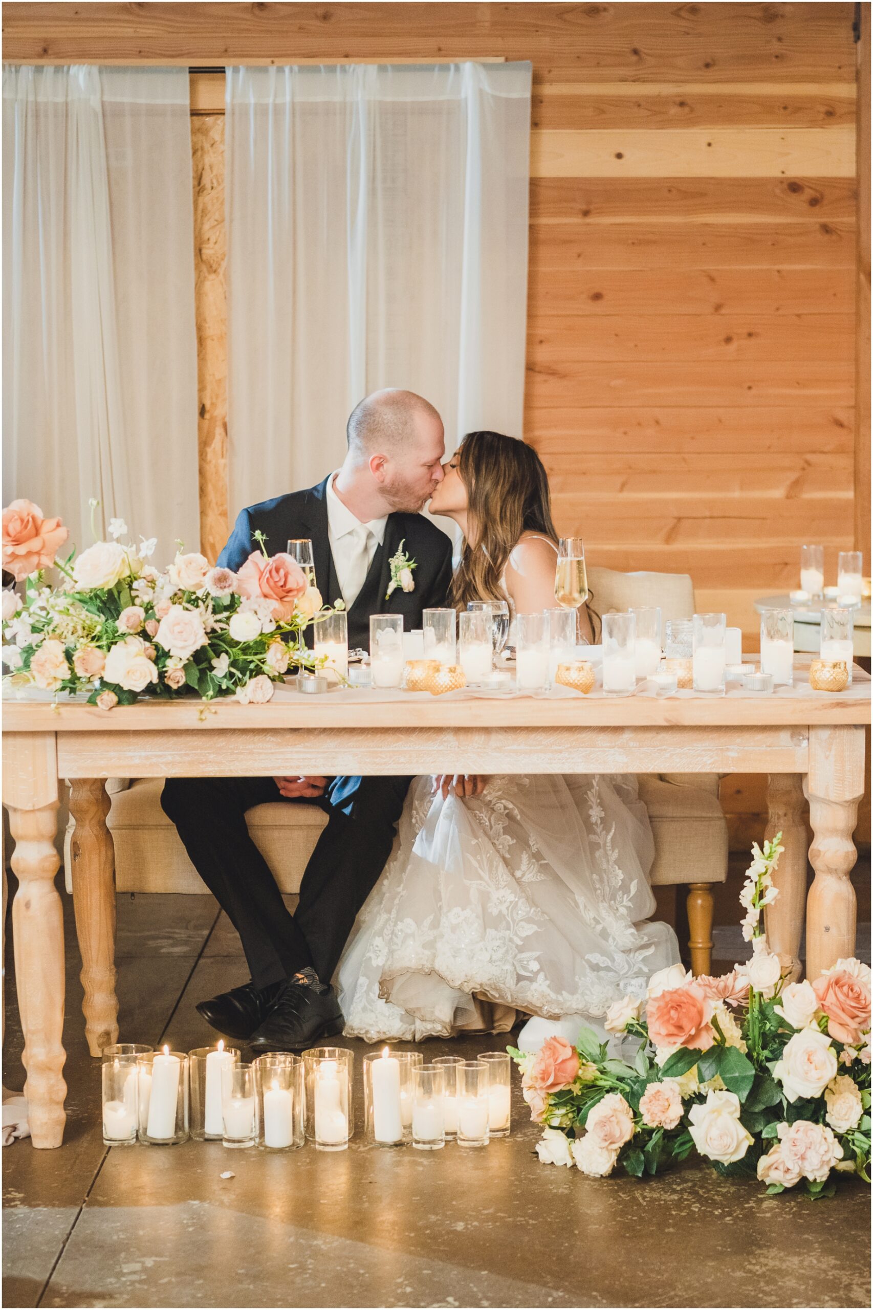 A wedding photo featuring a bride and groom kissing at their sweetheart table at Serendipity garden weddings