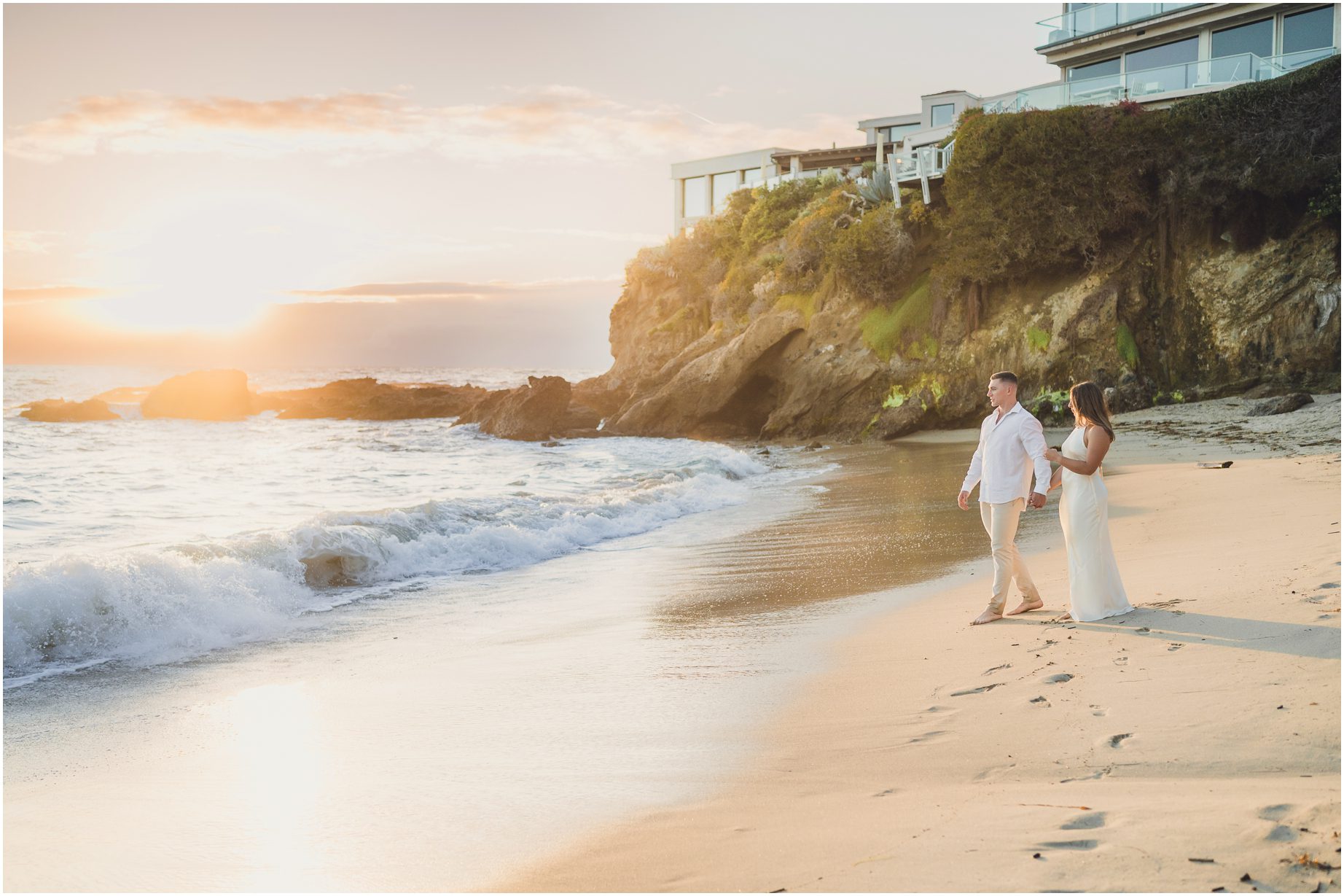 A couple in white, walking together at sunset for their Laguna Beach Engagement photos at Woods Cove