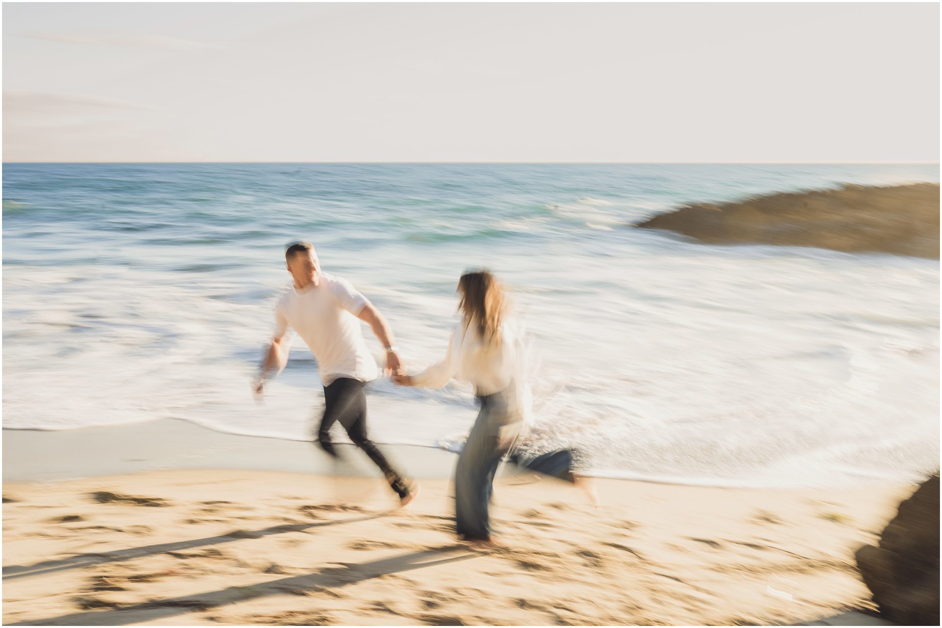 An engaged couple runs on the Beach at Woods Cove Laguna Beach