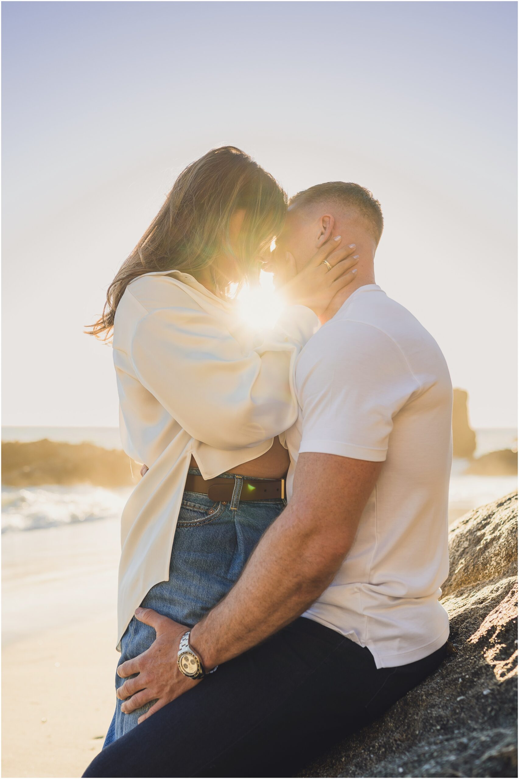 An engaged couple touches their foreheads together and the sun shines through them during their engagement photo session at woods cove in Laguna Beach