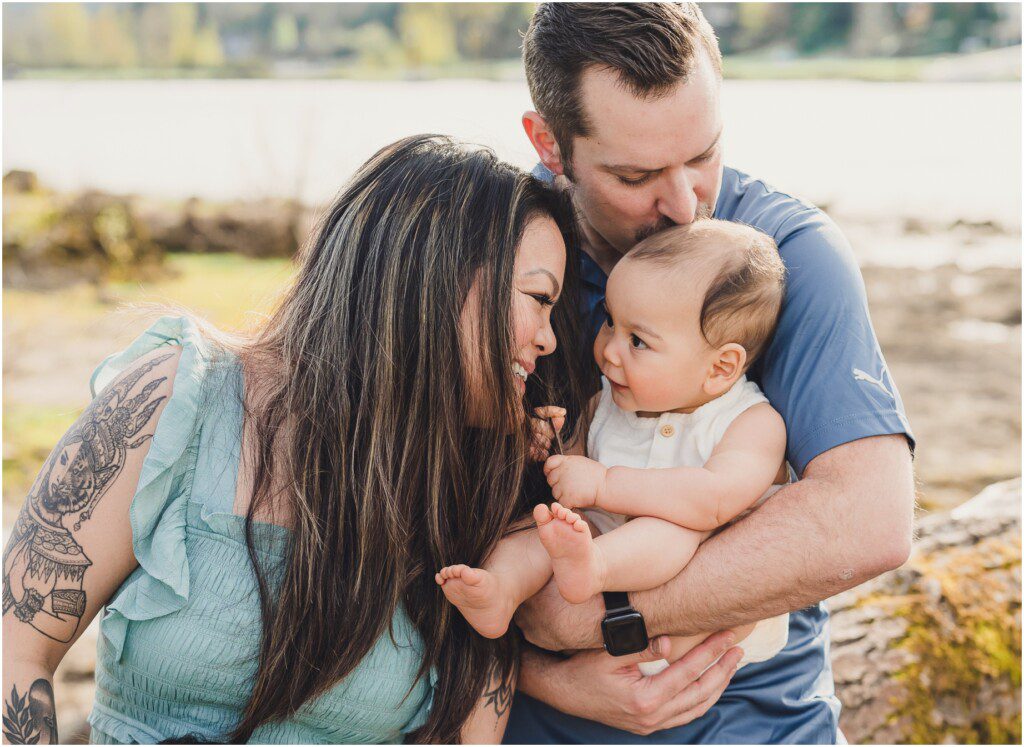 A mother and father hold their toddler and smile with him during a family photo session in Lake Oswego