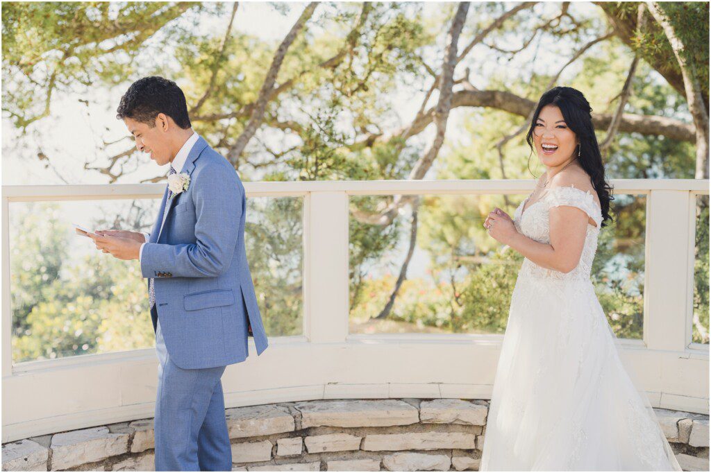A bride stands behind the groom, smiling, as he reads a note she wrote for him during their wedding at La Venta Inn The joy in this photo should be enough for anyone asking "should I have a first look at my wedding?"