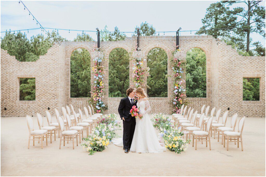 A bride and groom stand in a courtyard surrounded by flowers