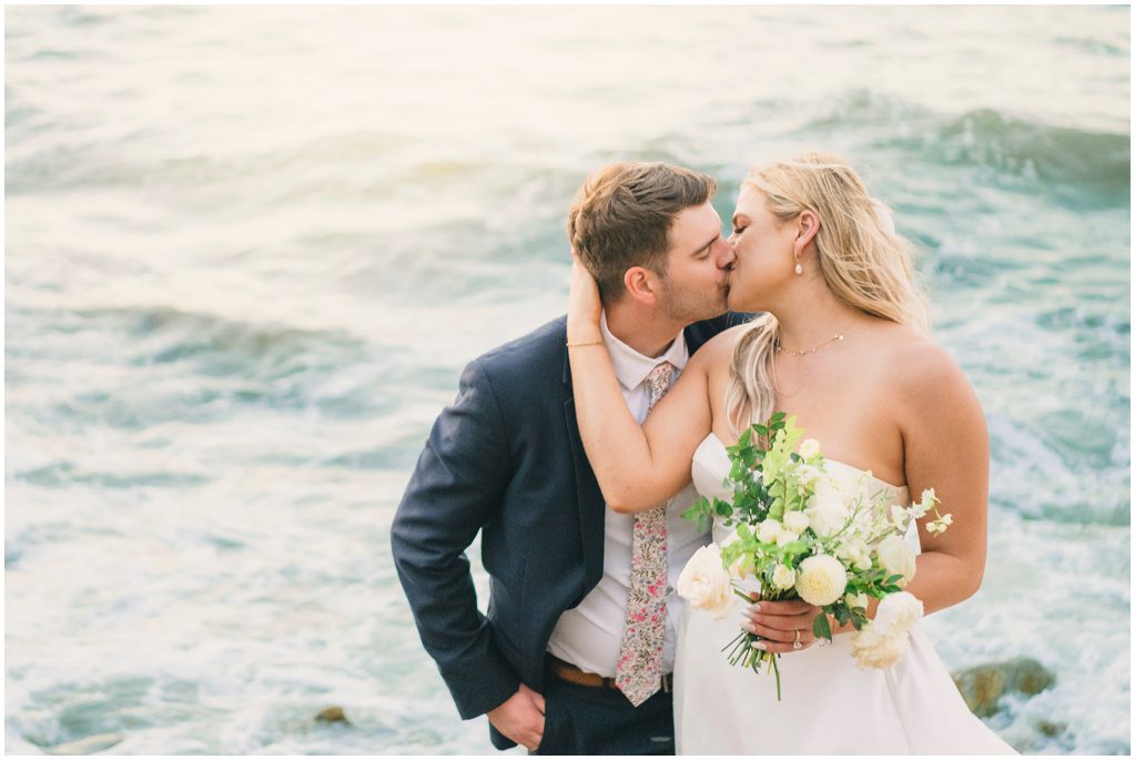 Bride and groom kiss over the ocean
