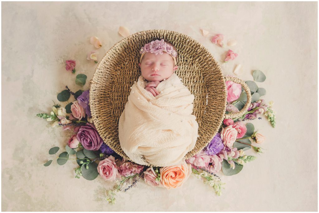 Baby laying in round basket with flowers around her for Manhattan Beach Newborn Photographer