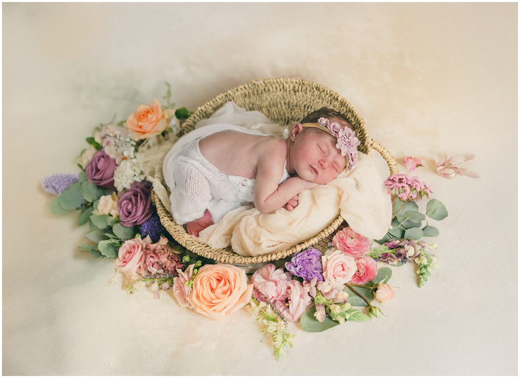 A baby lays in a basket surrounded by pastel flowers